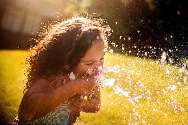 Dziewczynka w ogrodzie pijąca wodę z węża ogrodowego